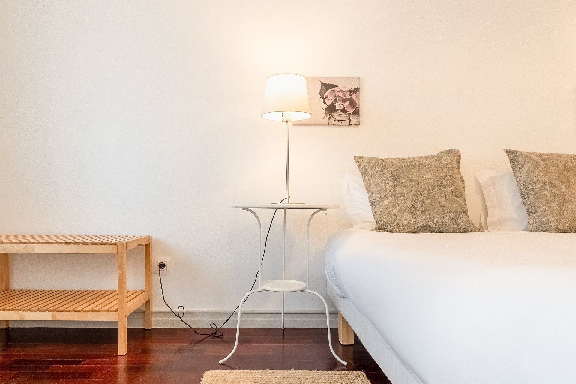 A bedroom with a bed, a bedside table, a floor lamp, and a wall-mounted picture.