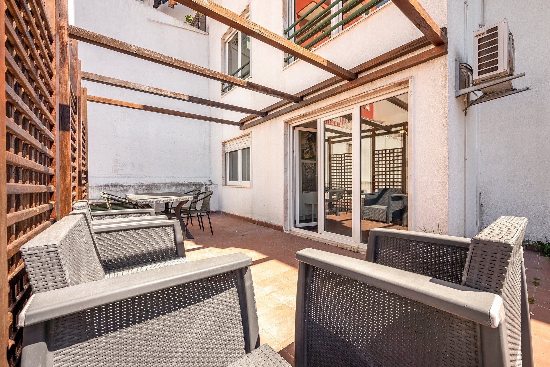 An outdoor patio area with wicker furniture, a wooden pergola, and a sliding glass door leading to an interior space.
