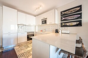A modern kitchen with white cabinets, a microwave, a toaster, and a patterned floor. - GuestReady - Stylish haven in Lisbon (Lisbon)