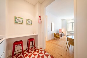 Ein modernes Interieur mit Küchenbereich, einem Essbereich mit Tisch und Stühlen sowie einem Flur mit geometrischem Fußbodenmuster.