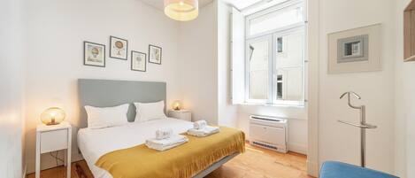 A hotel room with a bed, bedside tables, a window, a radiator, and a blue chair.
