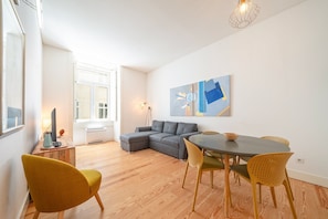 Ein modernes Wohnzimmer mit einem grauen Ecksofa, einem Esstisch mit Stühlen und einem großen abstrakten Gemälde an der Wand.