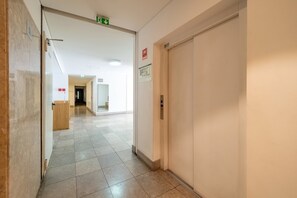 A hallway with a fire exit sign, an elevator, and a sign indicating a smoking area. - GuestReady - Modern home near Rua Augusta (Lisbon)