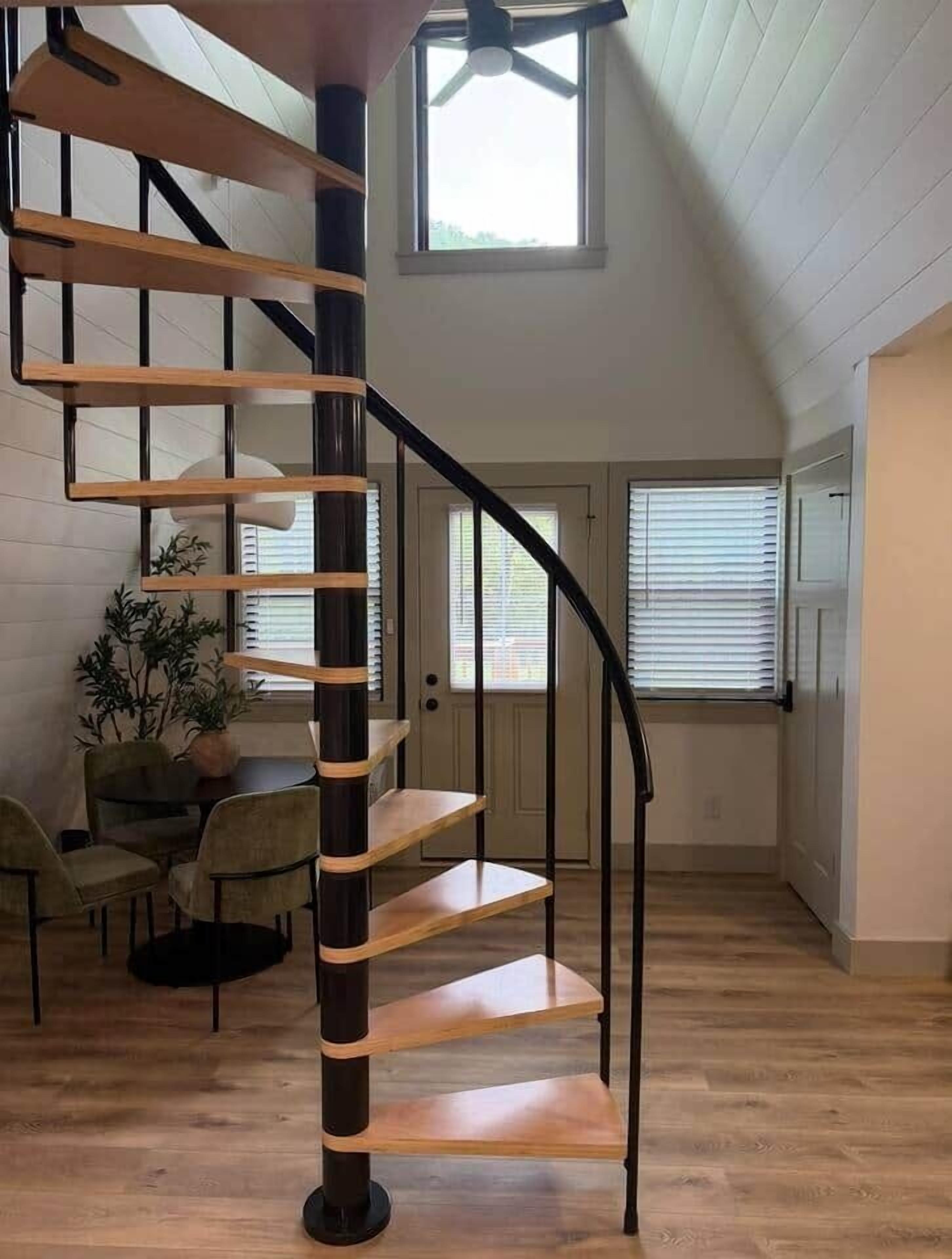 Eine Wendeltreppe mit Holzvertäfelung und schwarzen Metallgeländern in einem Raum mit hoher Decke und großen Fenstern.