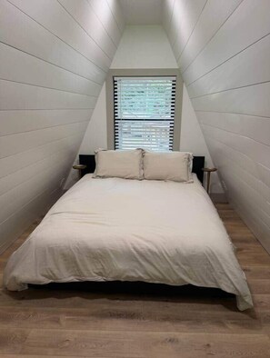 Een slaapkamer met een bed, een raam met zonwering en een nachtkastje.