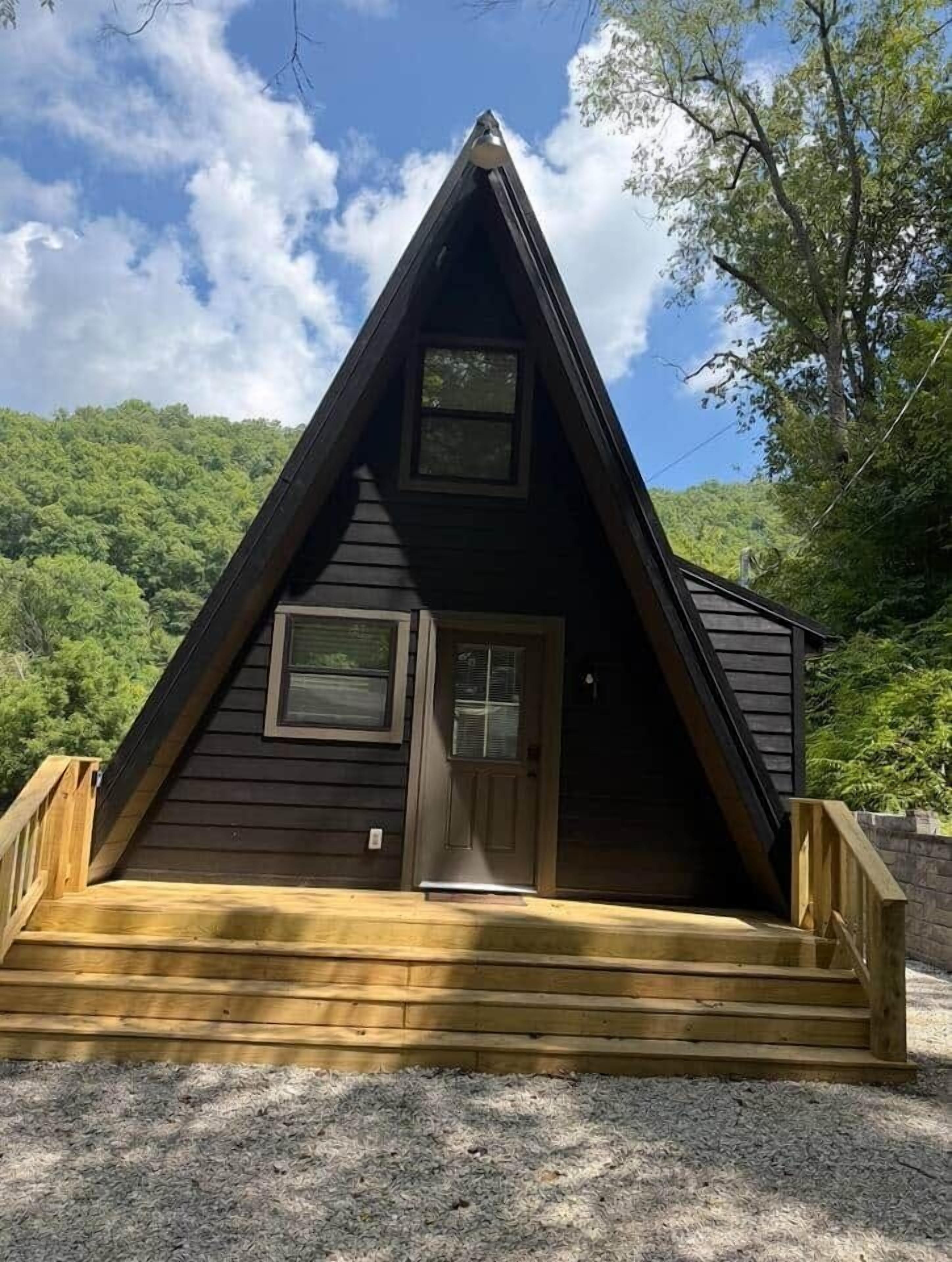 Une cabane en bois avec un toit triangulaire, une porte d’entrée et un petit porche.