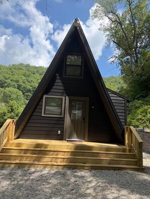 Een houten vakantiehuisje met een puntig dak, een voordeur en een klein terras.