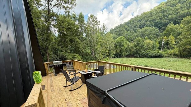 A wooden deck with a hot tub, outdoor furniture, and a view of a forested hillside.