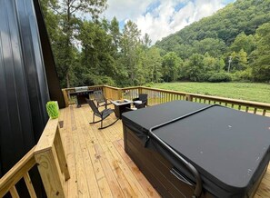 Een houten terras met een jacuzzi, tuinmeubilair en uitzicht op een bebost helling.