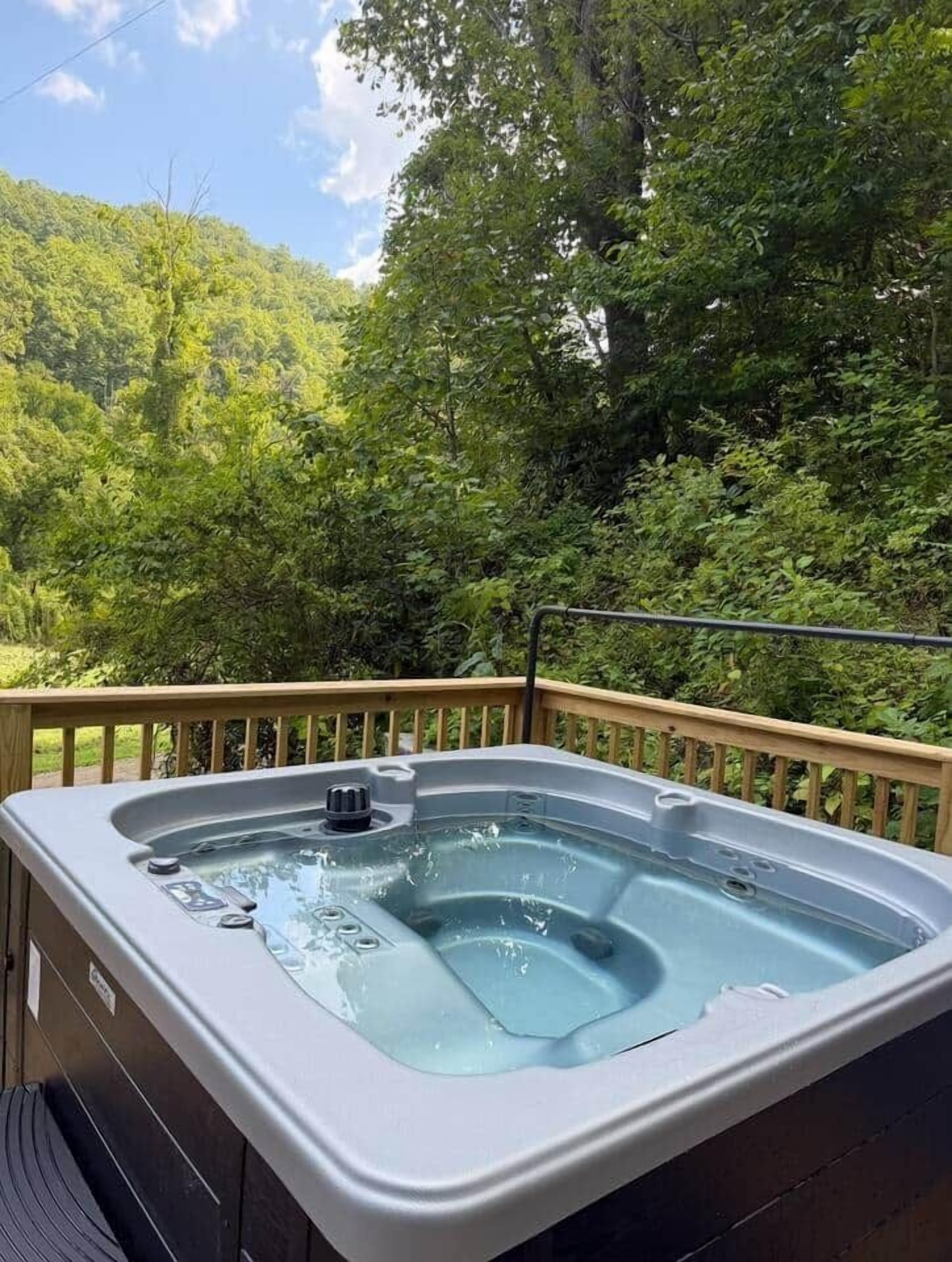 Un bain à remous sur une terrasse extérieure dotée d’une rambarde en bois, entouré d’une végétation luxuriante.