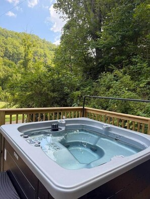 Een hottub op een terras buiten, met een houten reling, omgeven door weelderige begroeiing.