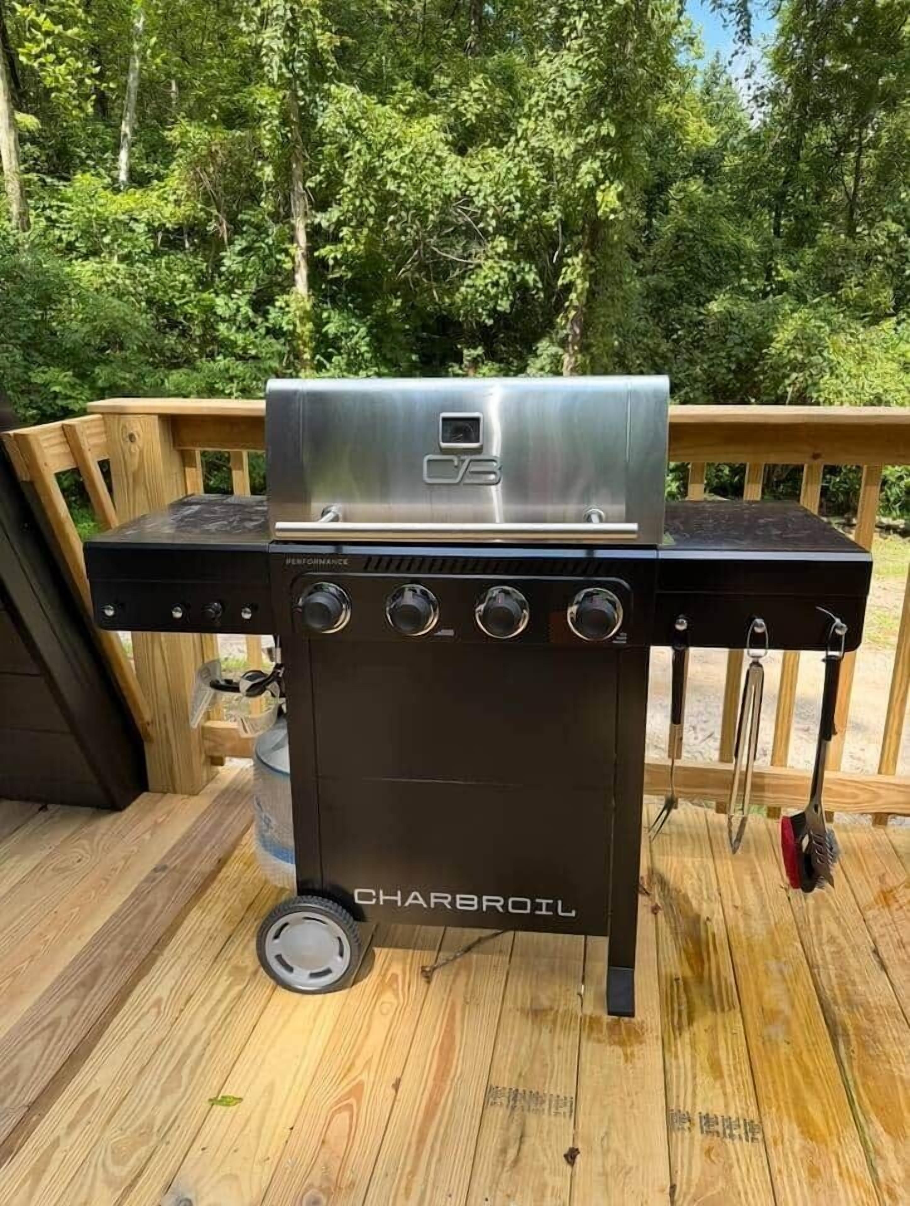 Un barbecue Charbroil doté d’un écran numérique, de plusieurs brûleurs et d’un brûleur latéral, installé sur une terrasse en bois avec un décor naturel en toile de fond.