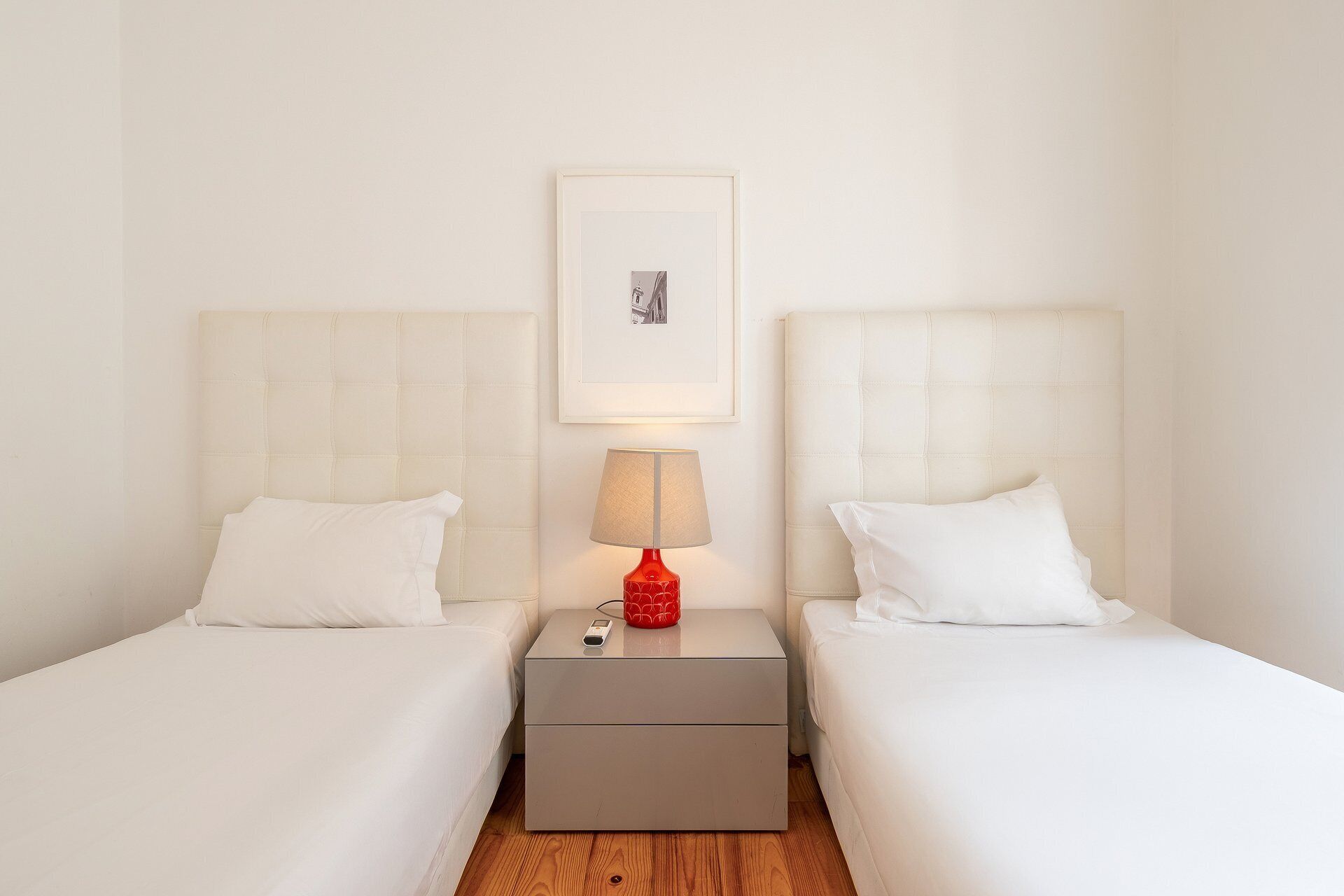 Ein Hotelzimmer mit zwei Betten, einem Nachttisch mit Lampe und einem gerahmten Bild an der Wand.