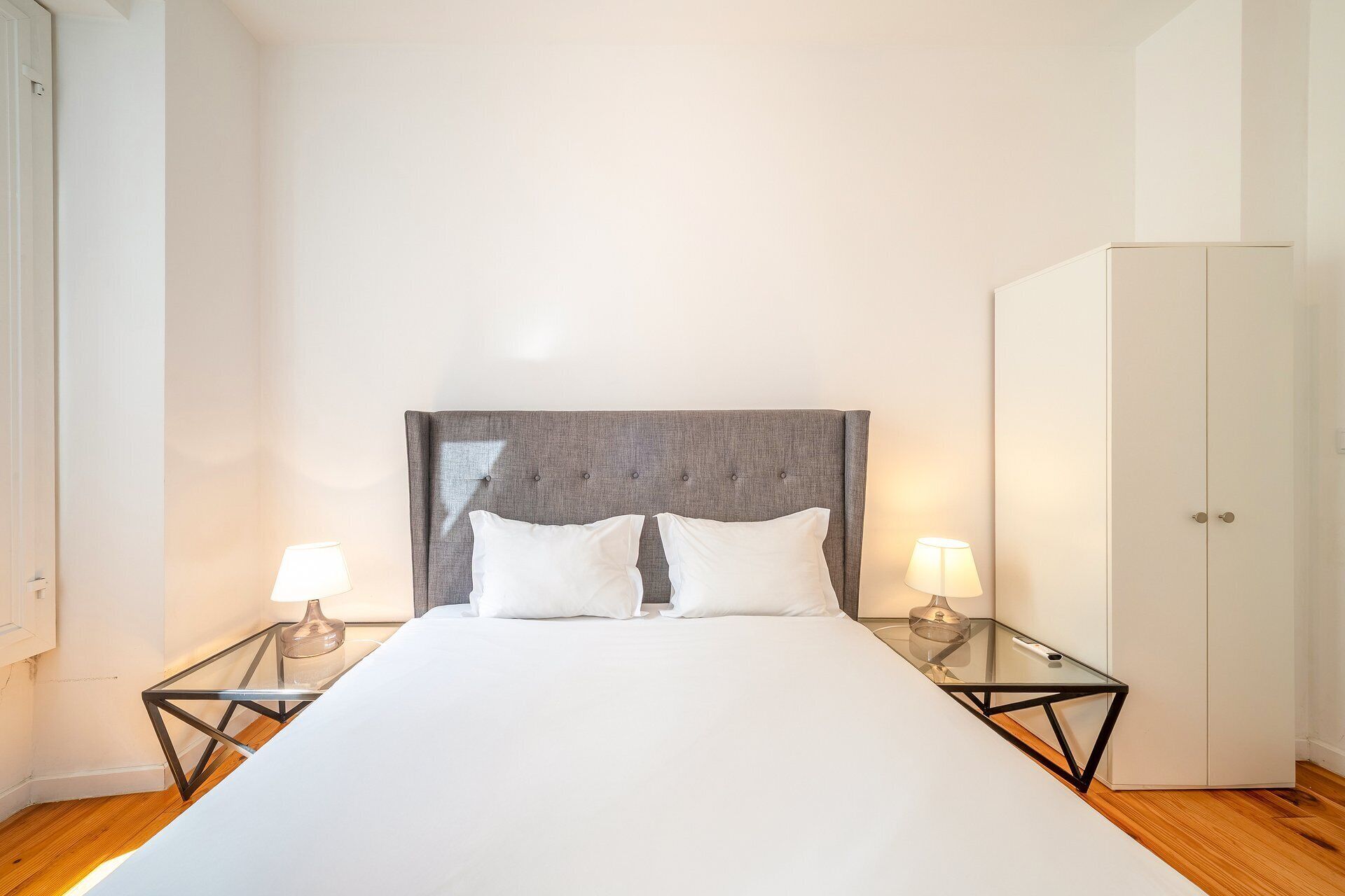 A hotel room with a large bed, two bedside lamps, a wardrobe, and a glass coffee table.