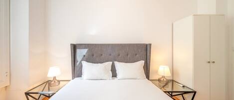 A hotel room with a large bed, two bedside lamps, a wardrobe, and a glass coffee table.