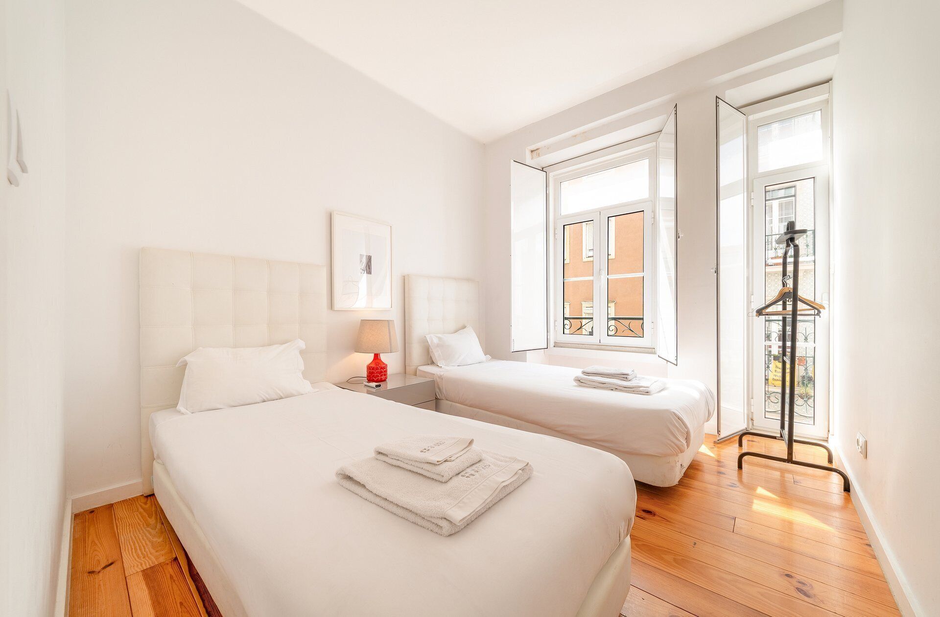 A hotel room with two beds, a window, a door, and a wooden floor.