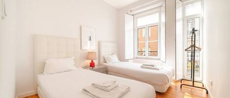 A hotel room with two beds, a window, a door, and a wooden floor.