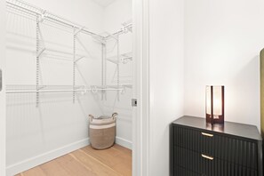 Een inloopkast met metalen schapunits, een gevlochten mand en een donkere dressoir met lades.