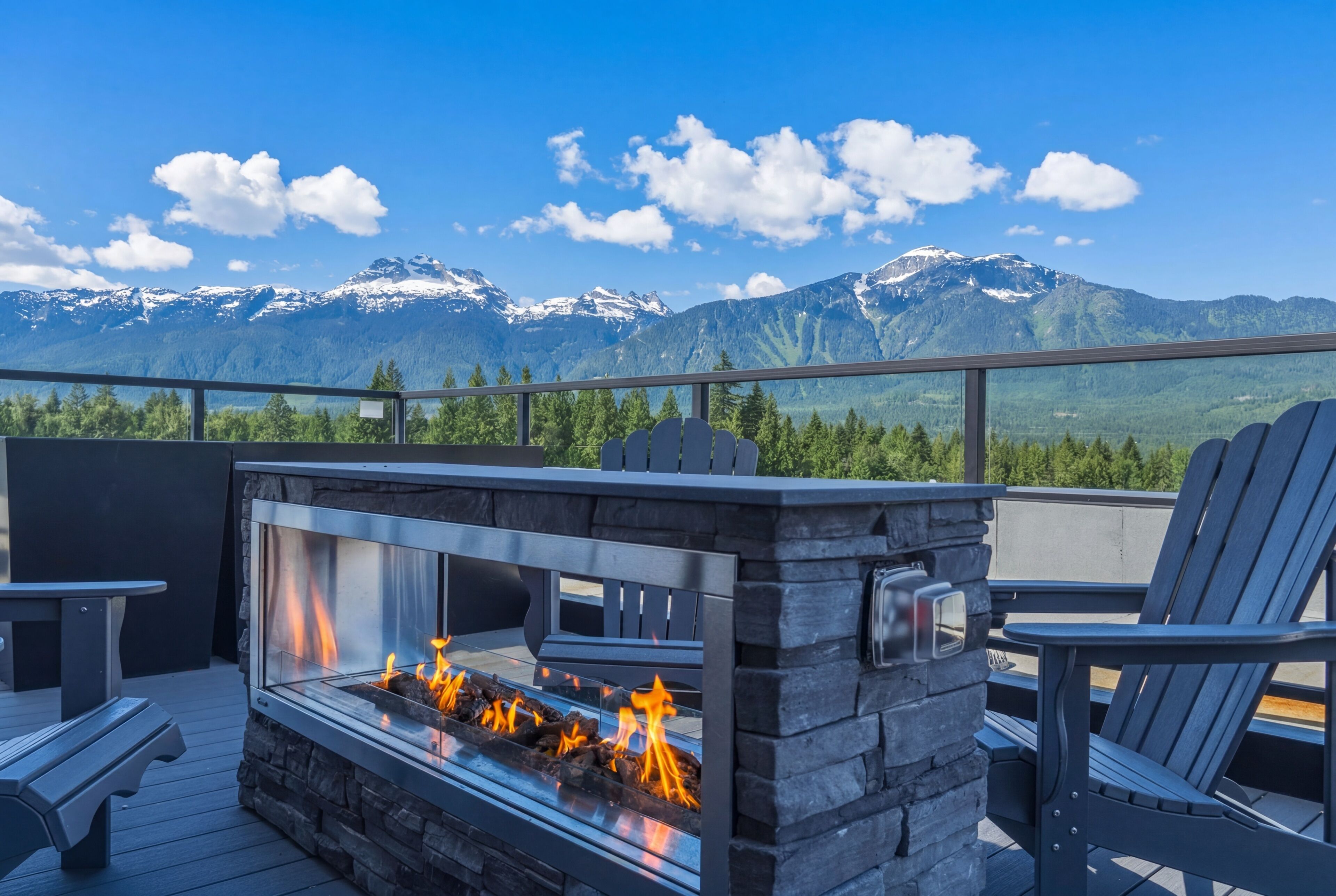 A stone fire feature with a glass enclosure, outdoor seating, and a mountain view.