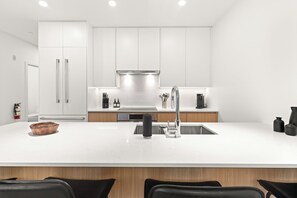 A modern kitchen with white cabinetry, a central island with a sink, and a stainless steel faucet. - Jalapeño Junction Cabin - 1300 sqft Townhome with Private Hot tub (Revelstoke)