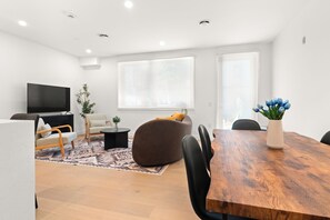 Een moderne woonkamer met een houten eettafel, een bank, een televisie en een groot raam.