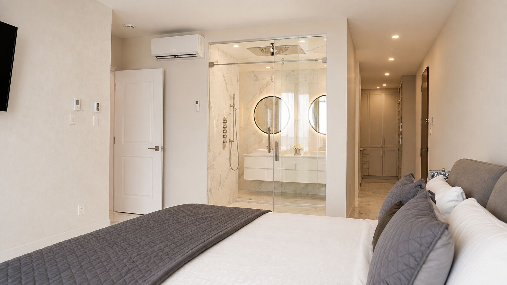 A bedroom with a bed, a shower area with glass doors, and a hallway leading to a bathroom.