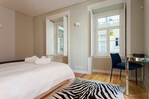 Een slaapkamer met een bed, een stoel, een bureau en een raam.