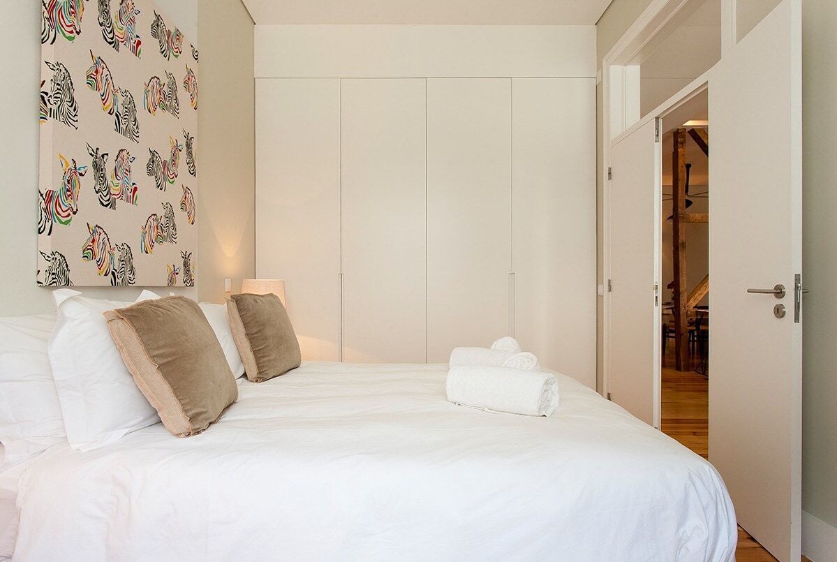 A hotel room with a bed, pillows, a wall with zebra patterns, and a door leading to another room.