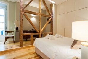 Une chambre à coucher avec un plafond en bois apparent, un lit recouvert de draps blancs, une lampe de chevet et une chaise.