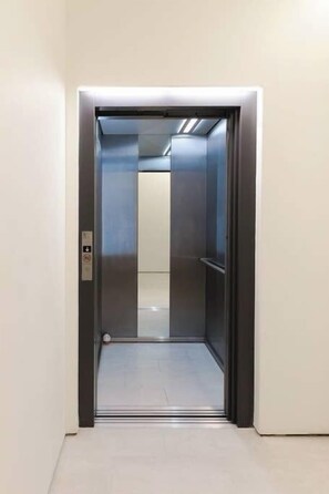 Ein Aufzug mit metallischer Innenraumgestaltung und Bedienfeld auf der linken Seite.