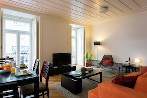 A living room with a dining area, a television, a sofa, and a small table with a lamp. - GuestReady - Sleek escape near Santa Justa Lift (Lisbon)