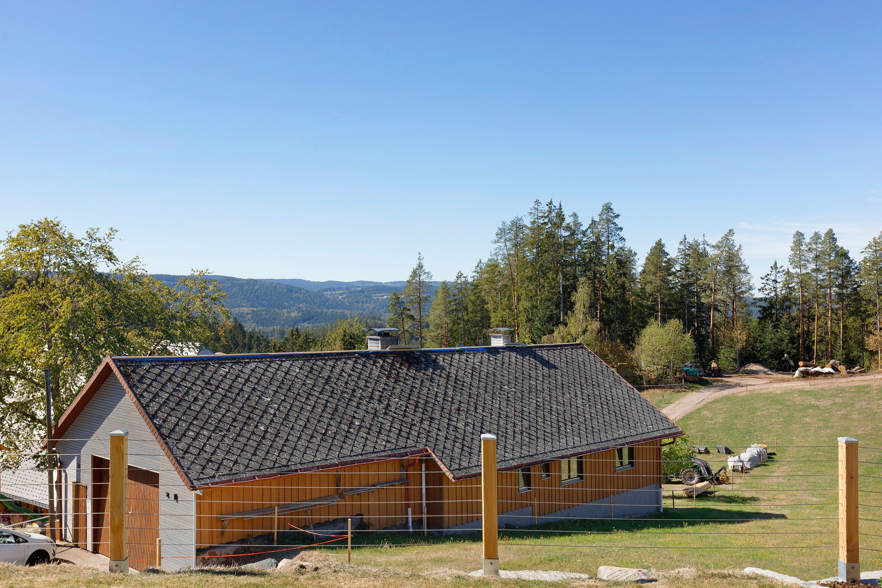Eine Holzhütte mit geneigtem Dach, umgeben von einem eingezäunten Garten und einer bewaldeten Landschaft.