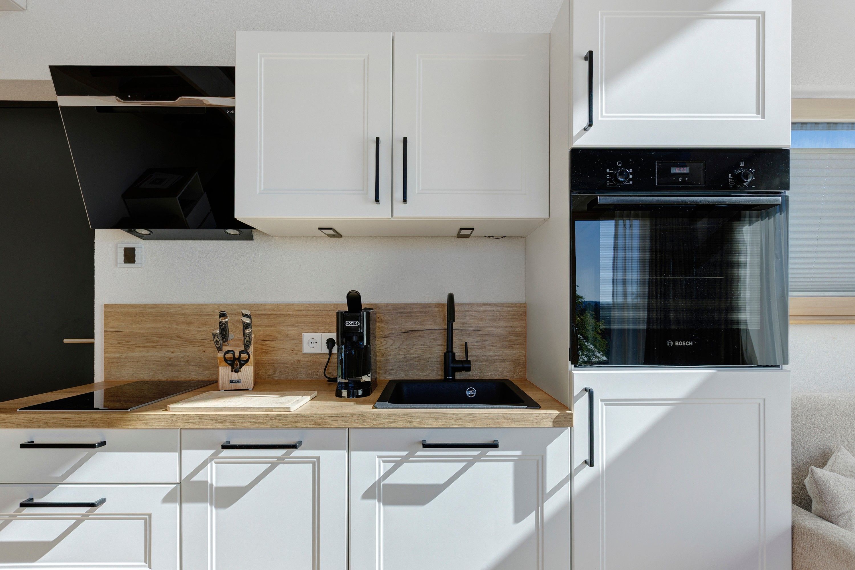 A modern kitchen with white cabinetry, a Bosch oven, and a coffee maker.