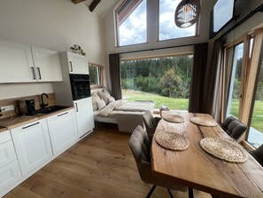A modern kitchen with white cabinets, a built-in oven, and a coffee maker. There is a dining area with a wooden table and woven placemats.