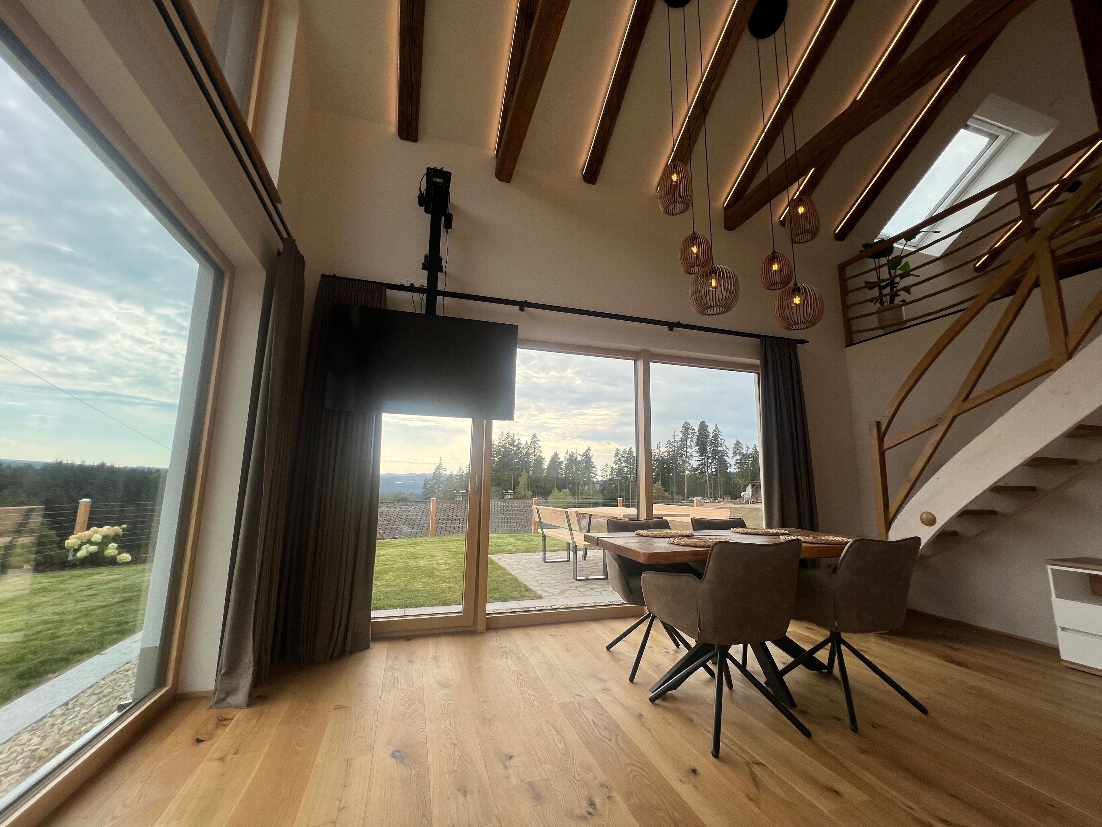 Ein modernes Interieur mit Essbereich, großen Fenstern und einer Treppe.