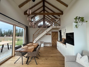 A modern kitchen with a built-in oven, a dining area with a wooden table and chairs, and a staircase leading to an upper level.