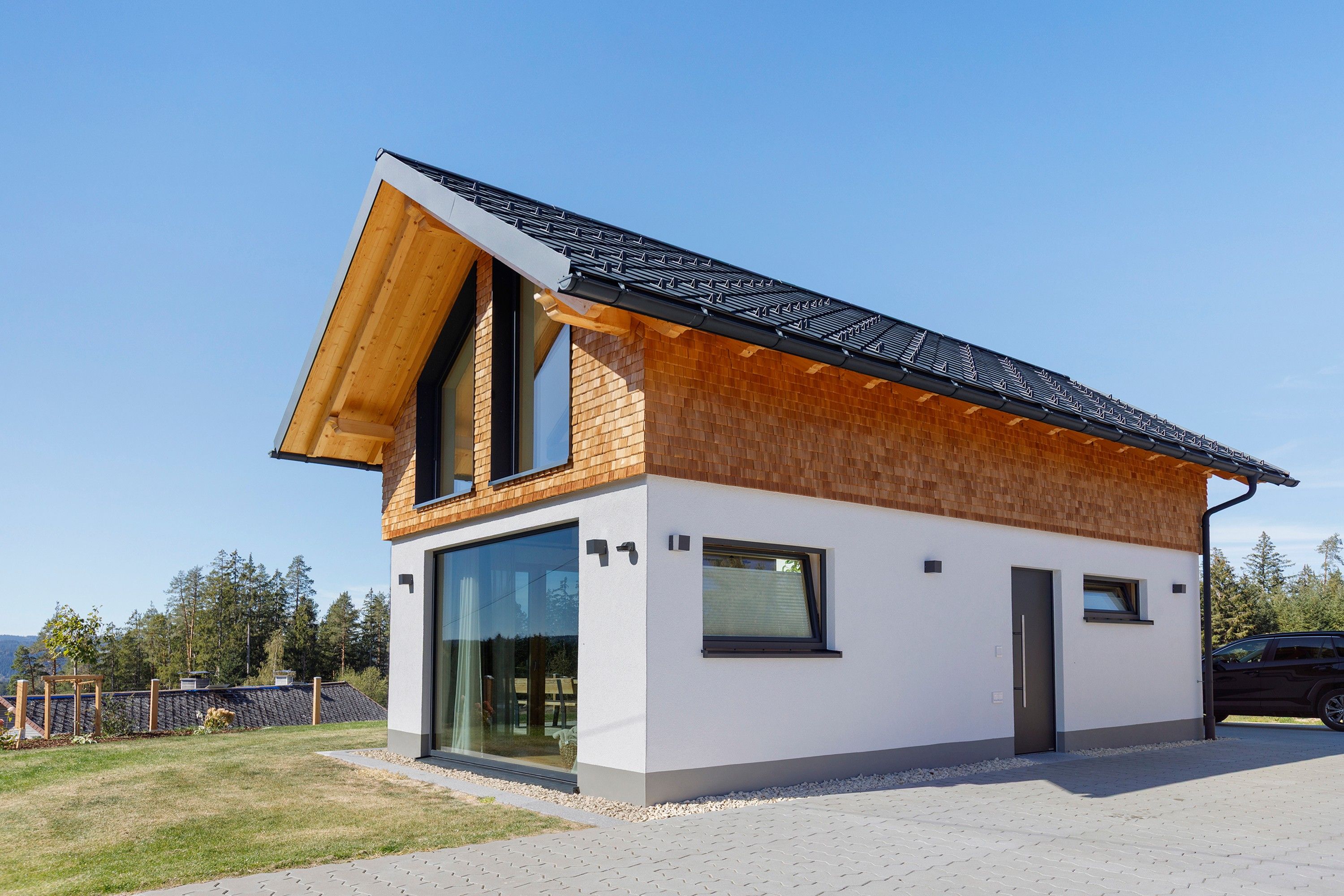 Une maison moderne à deux étages, dotée d’un toit en pente, de grandes fenêtres et d’une allée pavée.