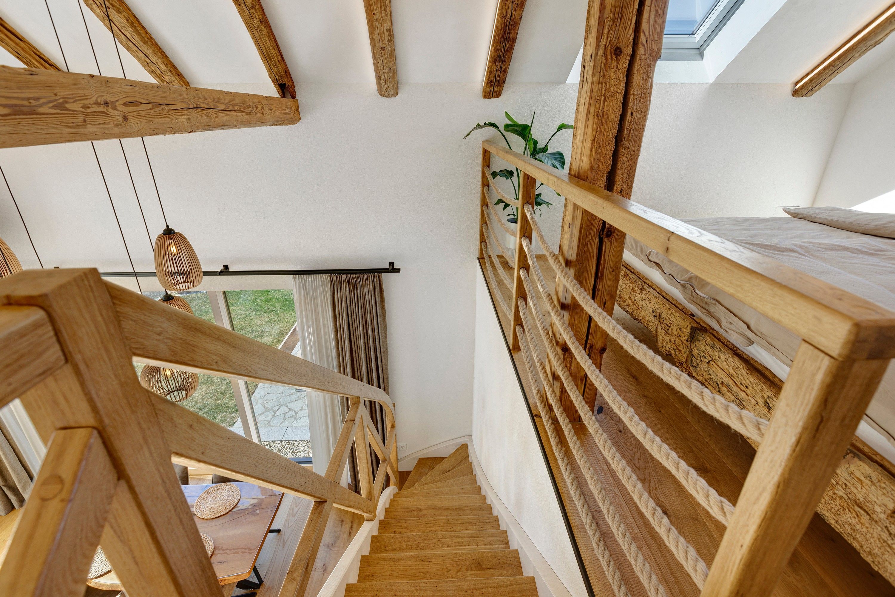 Eine Holztreppe mit Blick ins Freie, einer Pflanze und einem Fenster mit Vorhängen.