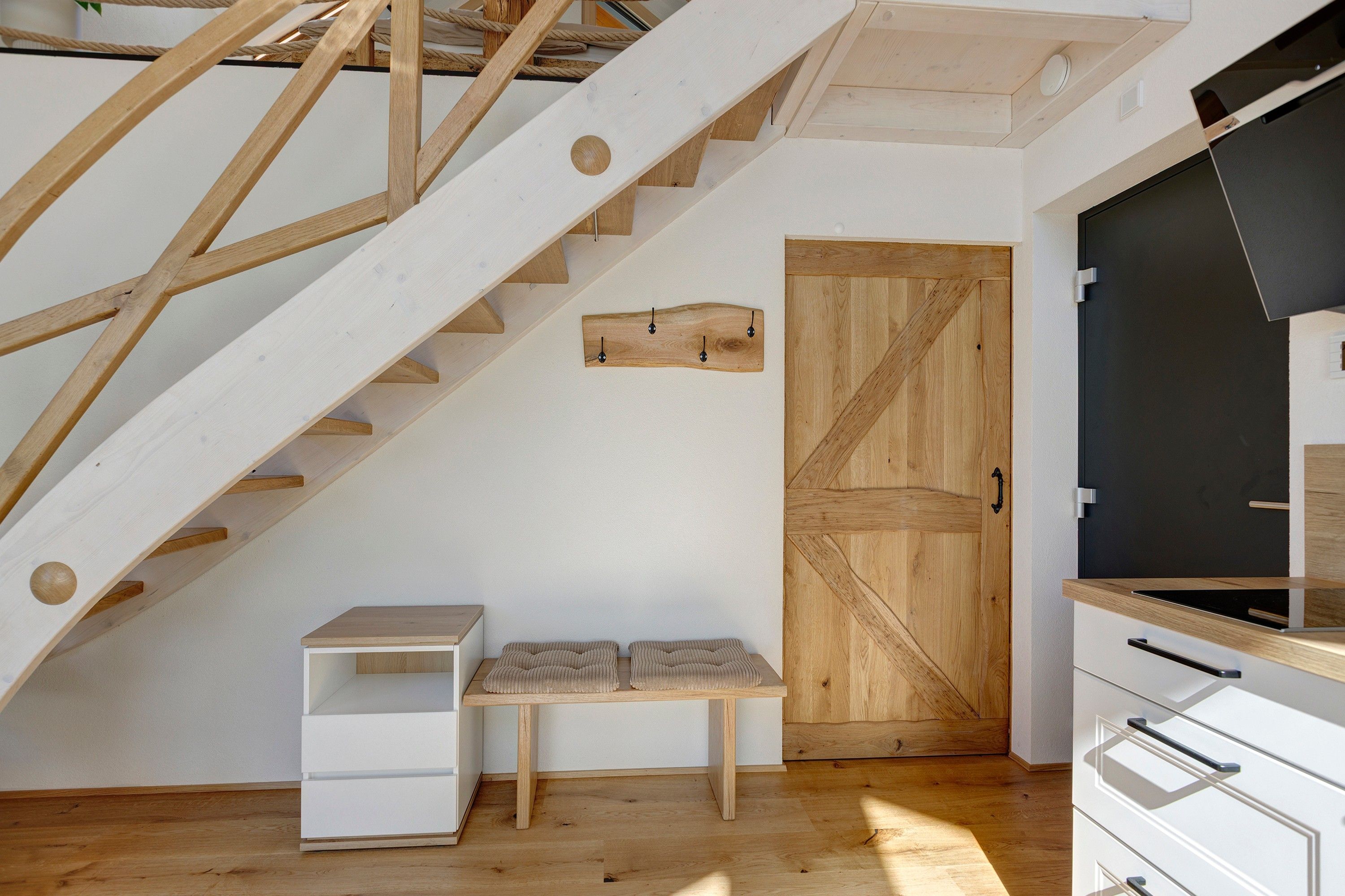 Ein modernes Interieur mit einer Holztreppe, einer Bank, einer Tür und einem weißen Schrank.