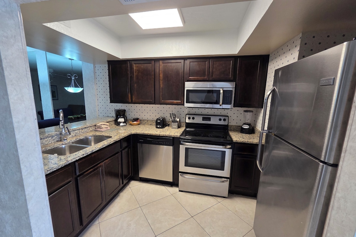 A modern kitchen with dark wooden cabinets, stainless steel appliances, a granite countertop, and a skylight.