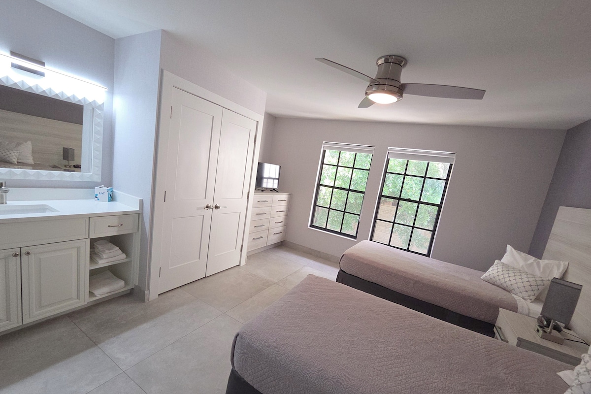 A bedroom with a bed, a dresser, a vanity, and a ceiling fan.