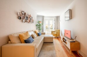 A modern living room with a sofa, armchairs, a TV, and a decorative wall piece. - GuestReady - Cosy stay near Money Museum (Lisbon)