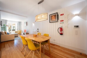A modern living room with a wooden dining table, yellow chairs, a fireplace, and a large window. - GuestReady - Cosy stay near Money Museum (Lisbon)
