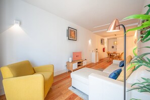 Een moderne woonkamer met een gele fauteuil, een witte bank, een flatscreen televisie en een eethoek met een tafel en stoelen.