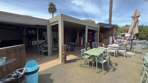 An outdoor dining area with tables and chairs, a trash bin, and a covered seating area. - Sweet 6-Person Mobile Home – Le Neptune 4* Campground (Argelès-sur-Mer)