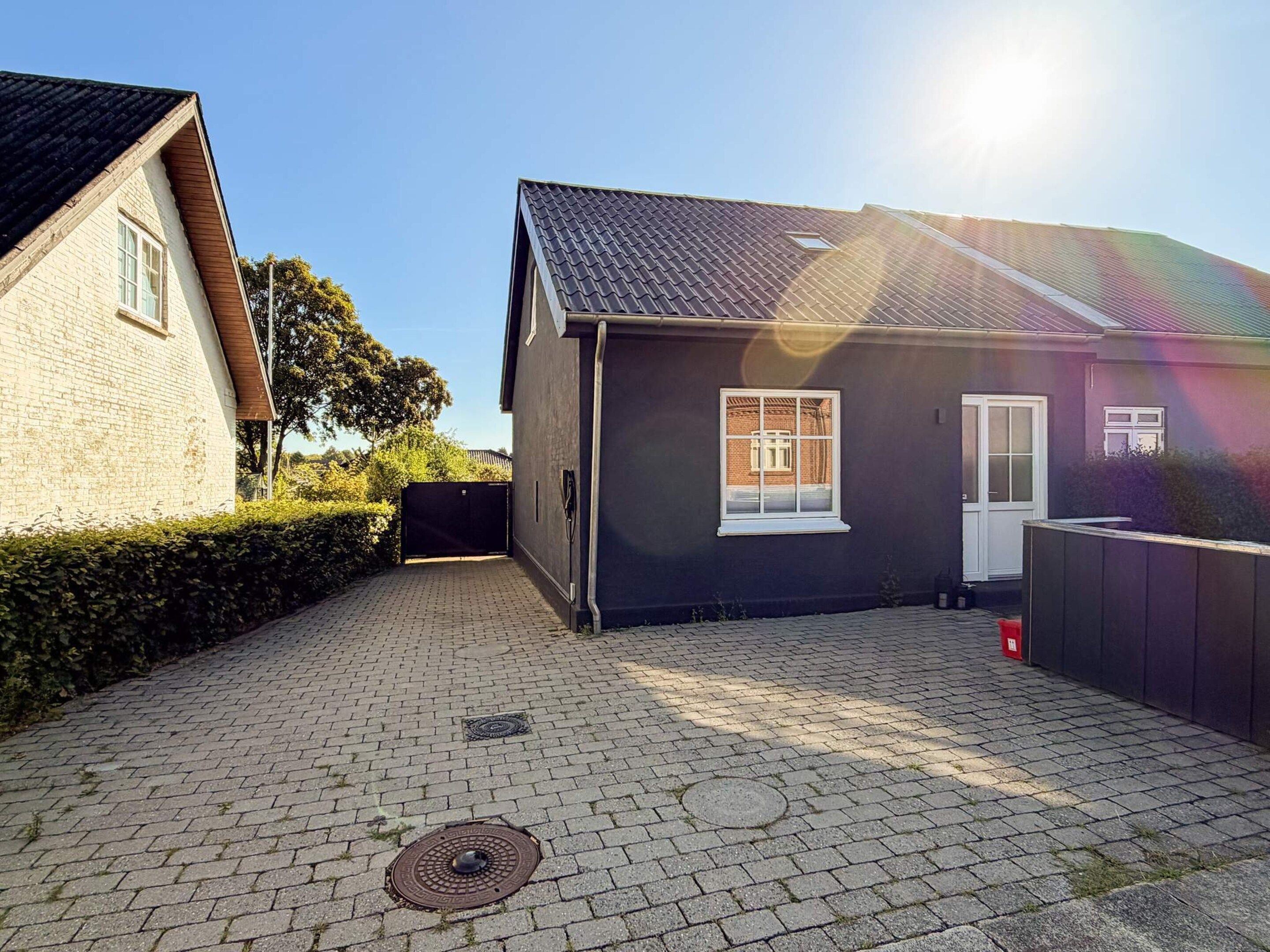 A residential property with a paved driveway, a black house with a white door, and a visible manhole cover.