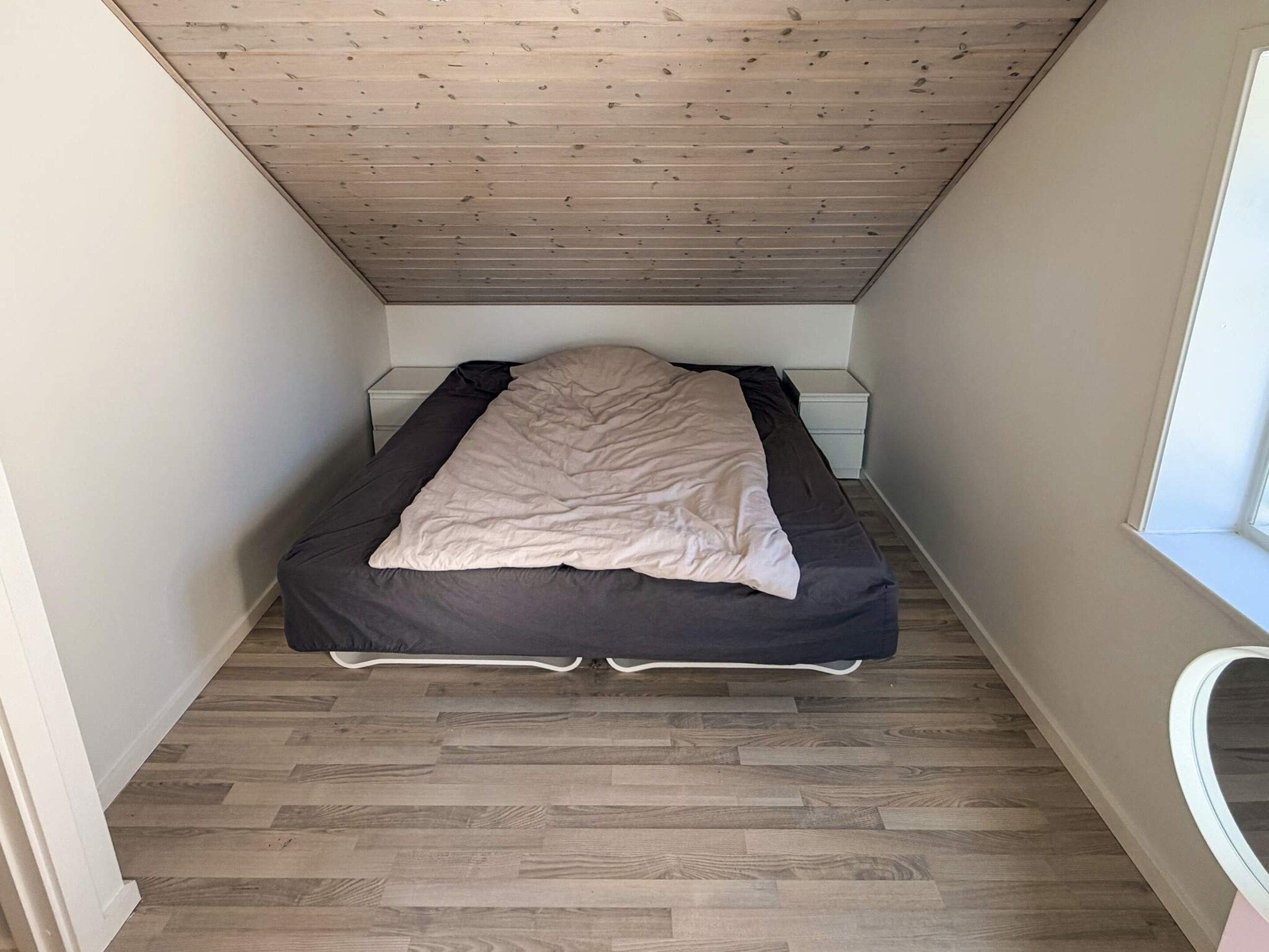 Een kleine, smalle kamer met een bed, nachtkastje en een raam.