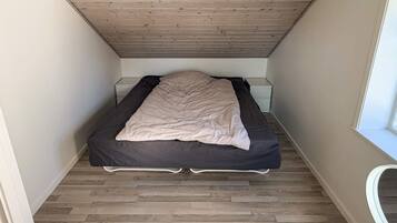 Een kleine, smalle kamer met een bed, nachtkastje en een raam.