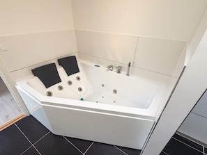A modern bathroom with a white bathtub, black bath mats, and a tiled floor. - 4 Star Holiday Home in Skanderborg (Skanderborg)