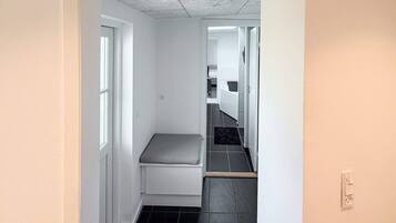 A narrow hallway with a bench, a door leading to a bathroom, and a tiled floor.